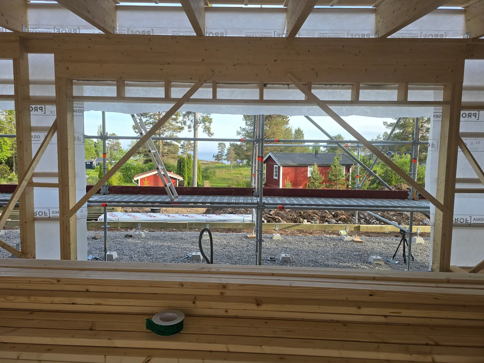 House framing with a view to water and a red cottage, before windows went in